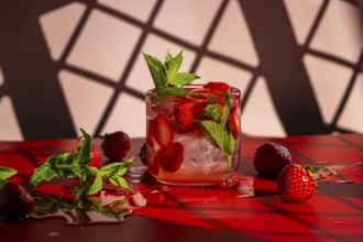 A vibrant strawberry mojito cocktail garnished with fresh mint leaves sits on a glossy red surface.