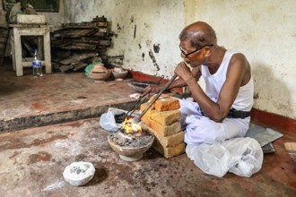 An old man works with fire and bricks in a workshop, he looks concentrated, a man burns sapphires