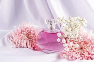A stylish perfume bottle filled with pink liquid is elegantly nestled among pink flowers and white