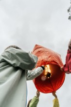 From below unrecognizable people in Taiwan lifting a glowing red Chinese lantern ready for flight.