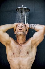 A man stands under a rainfall shower head, enjoying the refreshing flow of water. With closed eyes