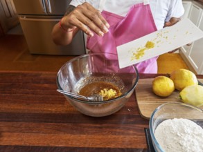 A woman wearing a pink apron prepares lemon cookies in the kitchen. She adds lemon zest to a brown