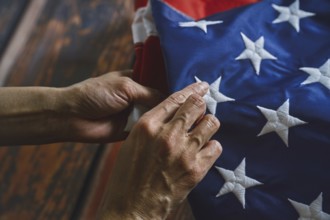 Close-up of hands reverently folding an American flag, emphasizing intricate stitching and vibrant
