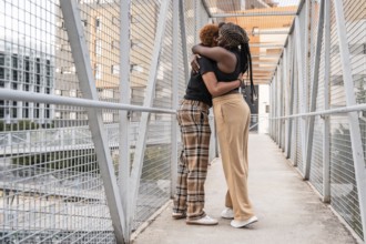 A loving LGBT multiethnic couple embraces on a metal bridge in an urban setting. Their warm hug