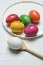 Coloured eggs on a plate and uncoloured eggs on a spoon, Easter celebration