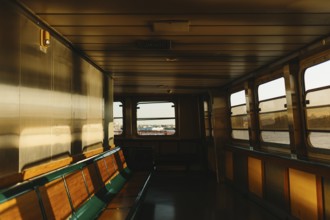 Warm sunlight illuminates the empty seats of a ferry interior, casting soft shadows in New York.