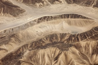Aerial view of a dry, mountainous desert landscape with sandy shades of brown, the landscape and