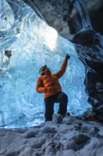 A man in an orange jacket in a glacier cave in Iceland in winter