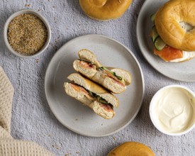 A top view of bagels with salmon and cream cheese on a speckled plate. A bowl of cream cheese and a