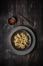 View from above of a plate of chili wontons on a wooden table next to chopsticks
