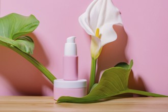 Pink skincare cosmetic products displayed with lush green leaves and a white calla lily against a
