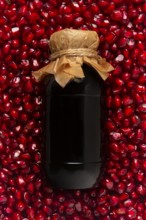 Pomegranate sauce in a bottle, top view, in pomegranate seeds, food background, vertical, no people