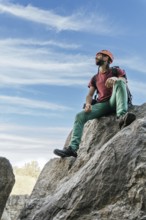 Young man with safety helmet and climbing equipment resting at the top of the mountain