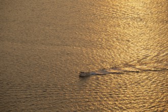 A small boat glides through the shimmering golden waters of the Mediterranean Sea at sunrise,