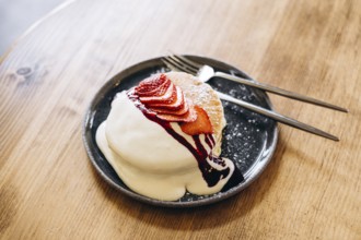 Fluffy japanese pancakes topped with fresh strawberries, a drizzle of cream, and berry sauce.