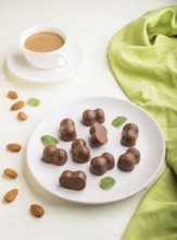 Chocolate candies with almonds and a cup of coffee on a white wooden background and green textile.