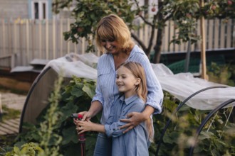 A joyful mother daughter duo tends to their greenhouse, surrounded by lush plants. They share a