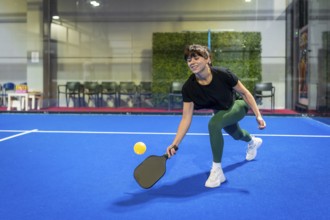 Woman playing pickleball on a vibrant blue indoor court, hitting the ball with her paddle during
