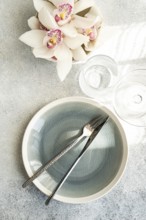 Stylish table setting features a textured ceramic plate, shiny cutlery, and delicate orchid flowers