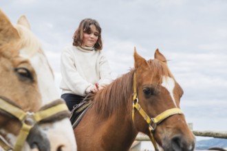 Young girl enjoying a peaceful day at the farm, sitting atop a horse. The clear sky and gentle