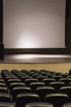 Rows of empty convention center seats facing a blank stage with a large screen, creating a quiet