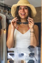 Happy tourist wearing straw hat trying on sunglasses in a souvenir shop in siargao island,