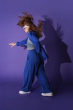 A young woman dances energetically against a vibrant purple background. Her dynamic pose and