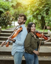 Portrait of two young violists back to back outdoors. Portrait of smiling male and female violinist