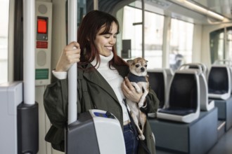 Smiling woman holding her chihuahua while riding on a tram. She wears a green coat and enjoys the