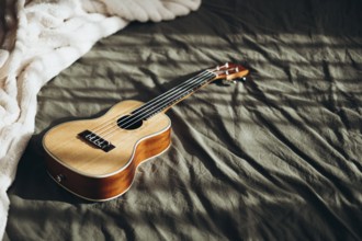 A wooden ukulele lies on a textured bedspread, illuminated by gentle natural light The warm tones