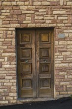 Distressed brown painted wooden entrance door on tan and beige cut stone residential building