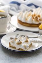A slice of homemade lemon cake with toasted peaks on a plate, paired with a cup of tea. The scene