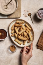 Top view of cropped unrecognizable hand holding a ceramic plate filled with sugar-coated churros,