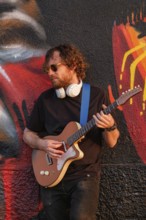 Hipster street musician in black playing electric guitar in the street on sunset leaning on a