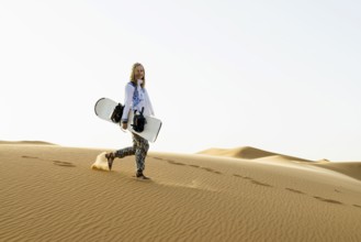 Young woman with snowboard in the sand dunes, near Merzouga, Meknès-Tafilalet region, Erg Chebbi,