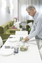 A man with intellectual disabilities carefully arranges dishes on a dining table in a supervised