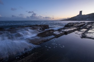 The serene sunset over the rocky coast of Tarifa, Cadiz, casts a soft glow on the water. Calm waves