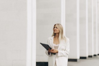 A professional woman holding a folder walks confidently beside a modern architectural structure.
