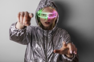 A woman wearing LED glasses and a metallic jacket poses against a neutral background. The bright