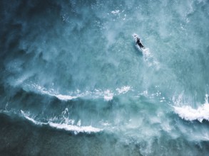Aerial shot capturing a surfer navigating the clear blue waves of Portugal. The image emphasizes