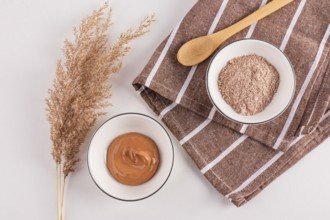 Top view of cosmetic clay powders in bowls beside an ornamental plant, presented with a wooden