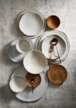 Top view of an assortment of ceramic and wooden plates and bowls arranged on a textured grey