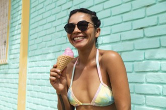 A joyful young Latin woman savors an ice cream cone under the sun in Mancora, Peru. Her bright