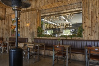 Warm, rustic cafe interior featuring wooden walls, vintage furniture, green plants, and a large