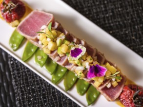 Exquisite sliced tuna tataki adorned with colorful edible flowers and diced fruit relish on a bed