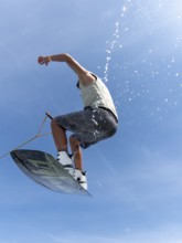 Young man jumping and flying with wakeboard, water sports and water skiing in the wakepark