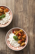 From above, two bowls of Hungarian pork goulash served with rice, garnished with a parsley leaf on