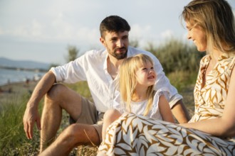 A loving family sits together on a peaceful beach in Italy, enjoying the warm summer air. The