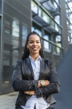 Vertical portrait of a proud latin businesswoman smiling with arms crossed standing in the city