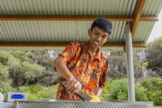 An Indonesian individual showcases vibrant batik clothing while cooking outdoors in Australia. The